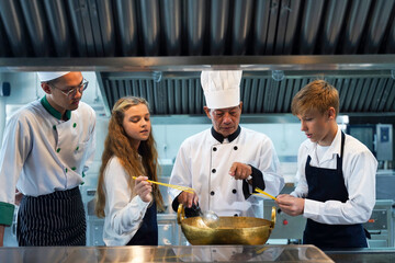 Chef teacher teaches cooking to the group children in class kitchen room.  Chef preparing student for learning marking and cooking food at workshop.  Education Concept