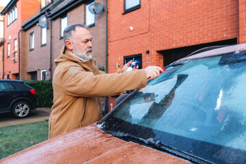 Man removes frost from car windshield in residential area during early morning hours