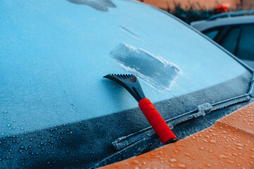 Frost scraper tool on ice-covered car windshield during winter morning in urban area