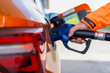 Fueling a car at a gas station with a person holding a gas pump in hand during daytime
