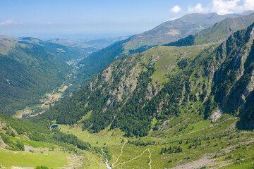 Fototapeta premium Aerial perspective of Espone Valley reveals steep forested slopes, rugged cliffs, and a winding stream under a clear blue sky. The vibrant summer landscape features layered textures and expansive
