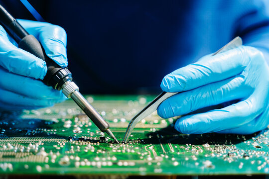 Close up of technician soldering and repairing circuit board in a modern laboratory, electronics repair, engineering, technology, maintenance and quality control concept. - Powered by Adobe