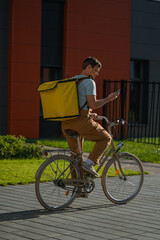 Bike courier on a city street riding a bicycle with a yellow insulated delivery bag, checking a smartphone for navigation modern gig economy food delivery, active and efficient