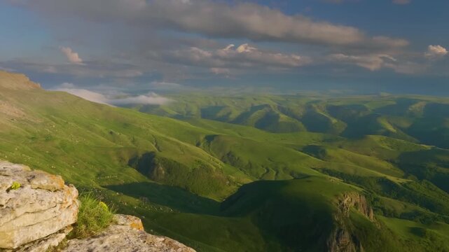 panoramic view of the vast, rolling green hills and mountain ranges in the North Caucasus region of Kabardino-Balkaria, Russia. The vibrant landscape is bathed in the warm, golden light of the late af