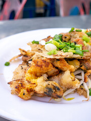 Fototapeta premium Crispy Thai Oyster Omelette (Hoi Tod) served with fresh bean sprouts and spring onions on a white plate
