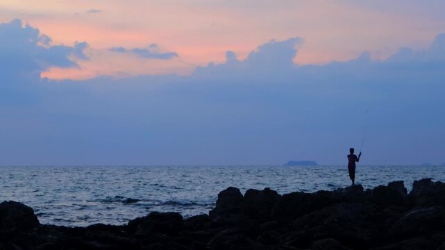 4K Wide silhouette shot of fishermen Catching fish standing on rocks in koh lanta , Thailand 