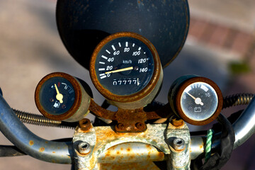 Close-up of vintage motorcycle dashboard with rusted gauges showing low fuel, low voltage, and 20 km/h speed—ideal for retro-themed background use and mechanical texture compositions.