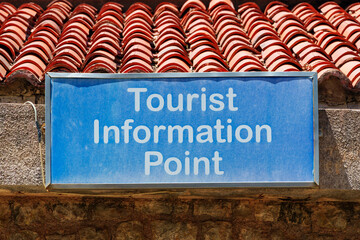 Blue tourist information point sign on a stone wall under a red tile roof in Petrovac Montenegro.