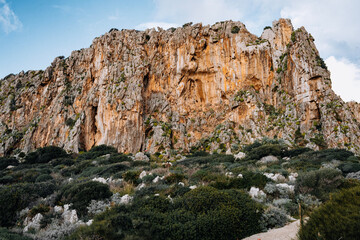 Limestone Rock Climbing Cliff In San Vito Lo Capo, Sicily: Steep Orange And White Coastal Crag Rising Above Mediterranean Vegetation Under Clear Sky