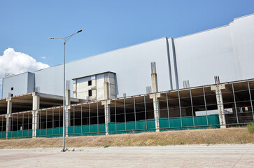 The progress of construction of a shopping center or warehouse. Construction site. Corrugated steel industrial building against blue sky