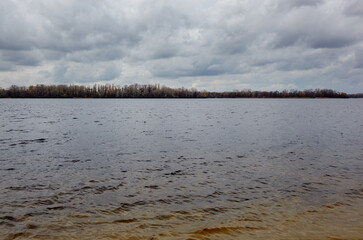 Lake surface on a bad weather day. Water against the background of trees and a sky before rainy