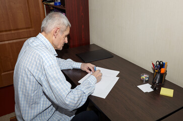 An elderly man writing letter. Man writing on a white sheet of paper with pen at wooden table