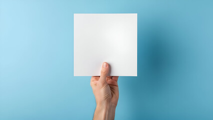 Fototapeta premium Clean design showcasing blank square paper held by hand against serene blue background