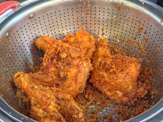 Golden-brown fried chicken pieces in a stainless steel colander.