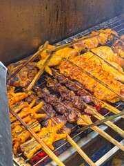 High-angle view of various chicken parts being grilled on a charcoal barbecue at a street food market.