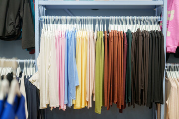 Shirts hanging on racks in a clothing store during the day with various colors arranged in order