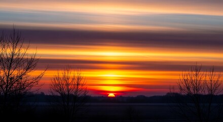 Obraz premium Vibrant sunset over horizon with silhouetted trees and colorful sky