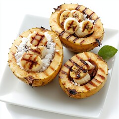 Three grilled pear halves filled with shredded coconut and banana slices are displayed on a white square plate with a small green leaf for decoration.