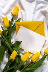 Bouquet of yellow tulips in craft paper bag on messy bed with white empty copy space postcard template. Romantic morning scene. Greeting card Holiday flowers springtime atmosphere