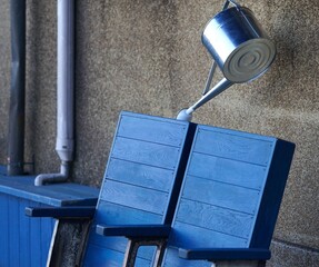 Blue chairs and a silver watering can. Blue wooden chairs leaning against a textured concrete wall