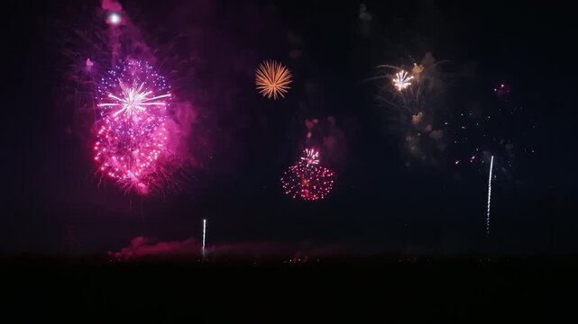 Colorful firework show over field at the celebration at the nighttime. People silhouettes are visible. Slow motion