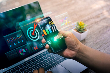 Business professional using smartphone and laptop with digital marketing analytics dashboard, advertising performance charts, data visualization, and mobile campaign management for online growth