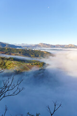 ronda,malaga,spain Morning fog filling a valley and obscuring the landscape, with mountains and a crescent moon in a clear blue sky