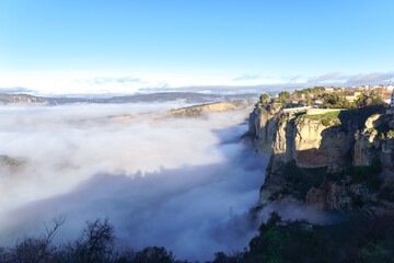 ronda,malaga,spain Ronda, andalusia. Fog rolls through el tajo gorge, revealing cliffside town and distant mountains under a blue sky