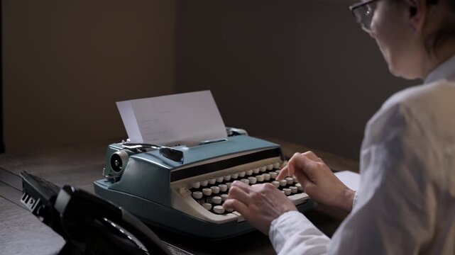 Person working on a vintage typewriter with paper inserted, struggling with sticking keys while typing. Answering a call on a retro telephone. 