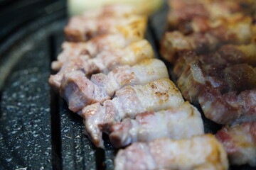 Sizzling Korean pork belly (samgyeopsal) grilling on a hot barbecue, close-up shot.
