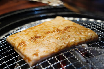 Korean style grilled pork skin sizzling on a charcoal grill, a popular anju snack