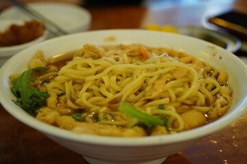 Delicious Korean style udon noodle soup with green vegetables in a white bowl, close up shot