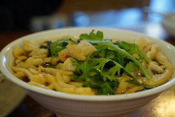 Delicious Korean style udon noodle soup with green vegetables in a white bowl, close up shot