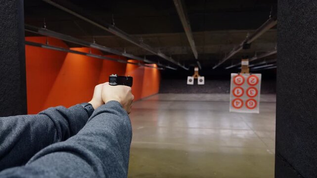 POV of person actively shooting a handgun at paper targets inside an indoor shooting range. Controlled firearm use, marksmanship training, and safe target practice.