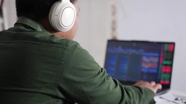 Over-the-shoulder view of a crypto trader analyzing crypto and stock charts live on a laptop using a trading platform application, with a happy and excited expression.  Stocks, and Crypto Trading.