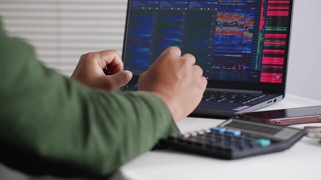 Over-the-shoulder view of a crypto trader analyzing crypto and stock charts live on a laptop, with a happy and excited expression. Concepts of Business, Stocks, and Crypto Trading.