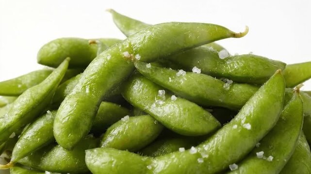 A vibrant close-up shot captures a delicious pile of freshly steamed green pods, commonly known as edamame, generously sprinkled with coarse sea salt. The crisp, verdant shells exhibit a natural gloss