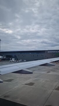 Iasi, Romania - December 12, 2025: Plane landing at Iasi International Airport. View from the window to the modern terminal facade. Ground crew are stationary as airplane moves from the runway