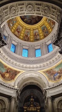 Breathtaking view inside the Saint-Louis des Invalides Cathedral in Paris, France. Massive circular ceiling of the dome adorned with golden Baroque paintings and intricate religious frescoes 