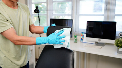 asian man cleaning and organizing an office desk with a computer and chair promoting tidiness and productivity