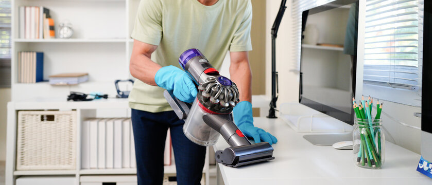 Asian man with handheld vacuum cleaning on Desk in home office.