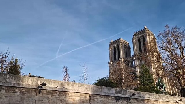 Scenic boat cruise along the Seine River in Paris, France with a view to the twin bell towers of the Notre-Dame Cathedral rising above a stone embankment