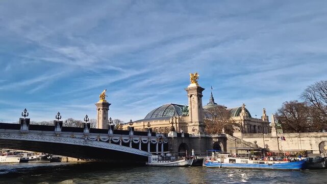 View from a cruising boat trip along the Seine river to the breathtaking Pont Alexandre III in Paris, France. The bridge is adorned with gilded statues. The Grand Palais with glass dome in background