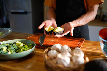 Male hands holding a fresh avocado cut in half with pit, over a wooden table. Healthy food preparation concept
