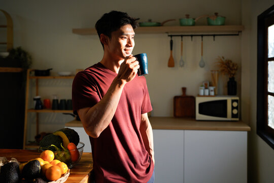 Portrait of smiling asian man drinking tea near the window at cozy home on winter morning.