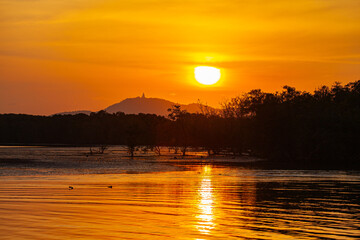 SceneryA tranquil sunset over a calm coastal landscape, with the golden sunset behind distant mountains and reflecting on the sea. The peaceful atmosphere is complemented by scattered rocks