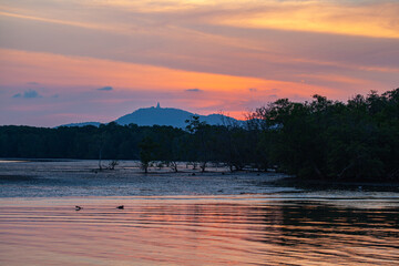 SceneryA tranquil sunset over a calm coastal landscape, with the golden sunset behind distant mountains and reflecting on the sea. The peaceful atmosphere is complemented by scattered rocks