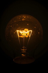 Closeup macro of glowing tungsten filament inside vintage light bulb in dark