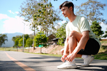 Young athlete man tying running shoes in the park outdoor, male runner ready for jogging on the...