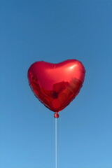 Fototapeta premium Single red heart shaped foil balloon floating against clear blue sky